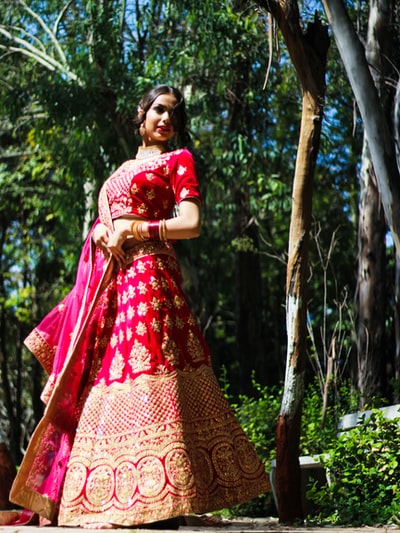 Standing beside the tree during the day to women who dress in red and gold sari
